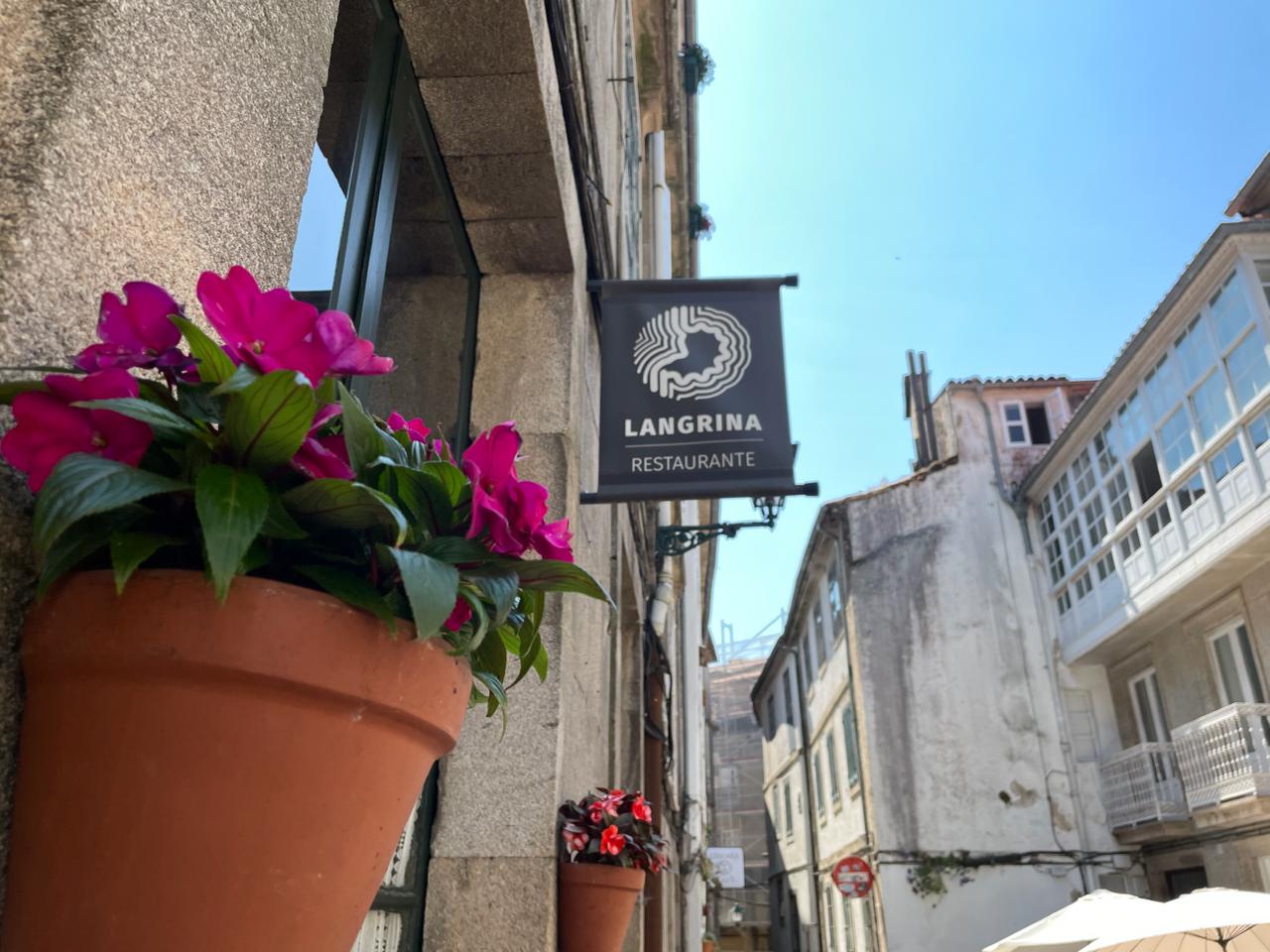 Cartel de Langrina con flores en la calle empedrada del casco vello